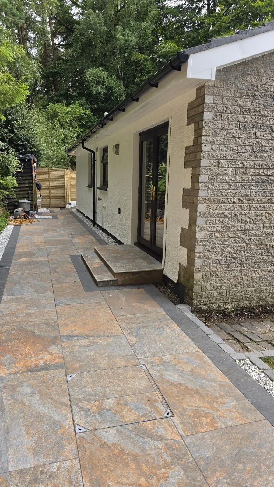 A stone-paved path along a white bungalow to black-framed glass doors, with a small step up.